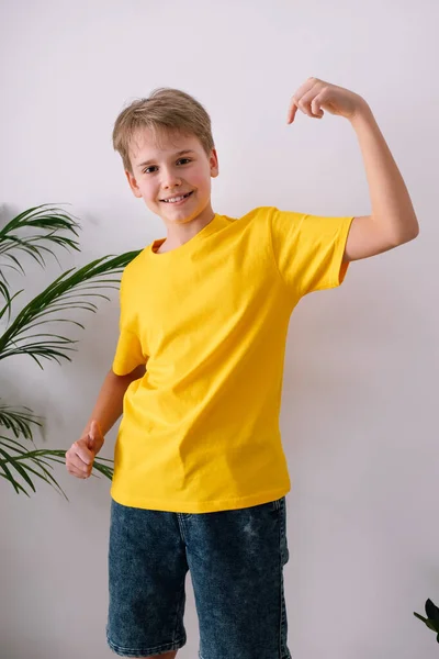 Szczęśliwy nastolatek celujący w koszulkę. Żółty t-shirt makieta — Zdjęcie stockowe