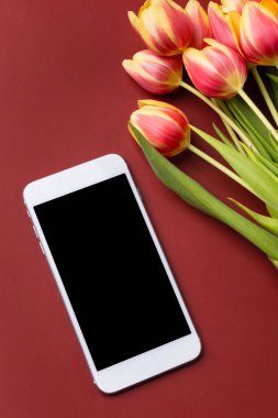 Boş ekranlı telefon ve kırmızı şarap arkaplanda bir buket lale. Akıllı telefon maketi.