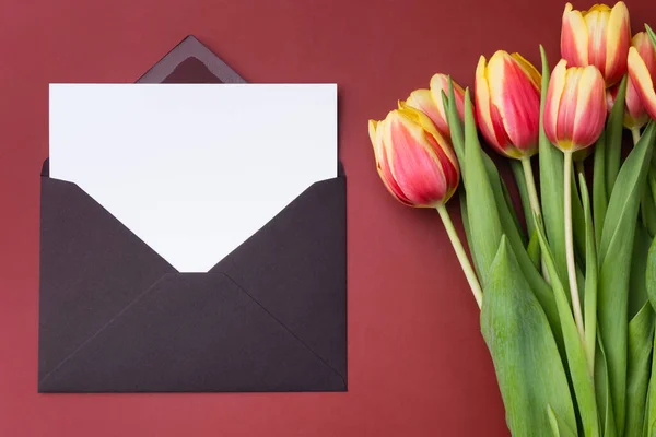 Білий горизонтальний макет карти або спасибі шаблон карти в конверті з букетом тюльпанів на бордовому фоні . — стокове фото