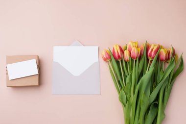 Tebrik kartı modeli ya da teşekkür kartı şablonu. Bir buket lale ve bej arka planda bir hediye kutusu..