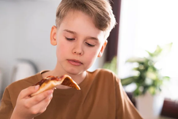 Nastolatek je pizzę siedząc w kuchni w domu. Szybki lunch. — Zdjęcie stockowe