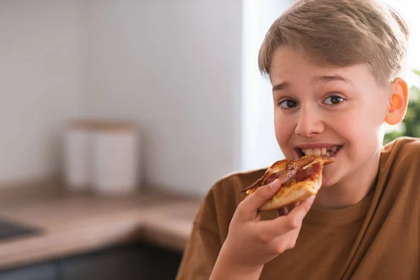 Happy teenager enjoying eating delicious pizza at home. Freshly baked pepperoni pizza — Zdjęcie stockowe