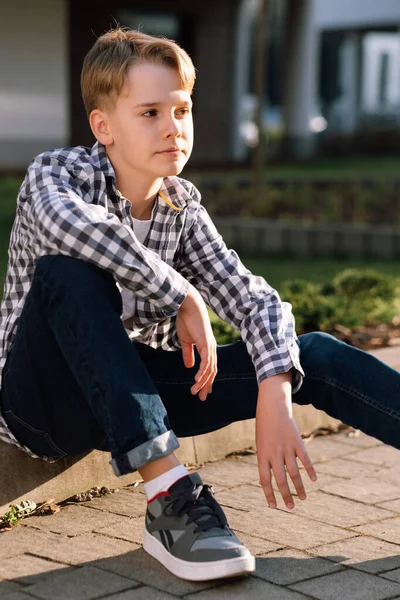 Stylish young guy teenager smiling while sitting on the curb outdoors. — Stok fotoğraf