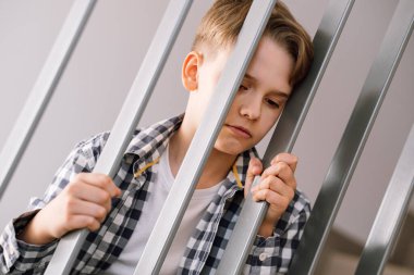 Kızgın ya da gücenmiş ifadesi olan genç bir adam parmaklıklara tutunuyor. Ergenlik sorunları, gençlik sorunları..