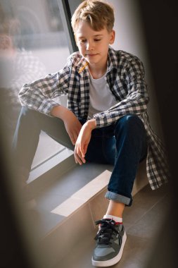 Genç bir çocuk pencerenin yanında yerde oturuyor. Şık bir genç bir şey düşünür ve gülümser. Modern gençliğin yaşam tarzı