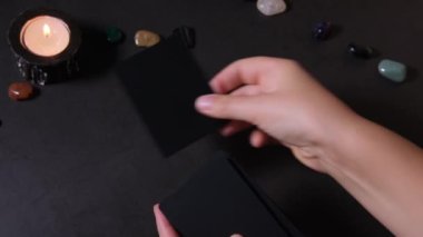 The hands of a fortune teller woman make a deal for the future with the help of a black deck of cards. Esotericism and tarot cards