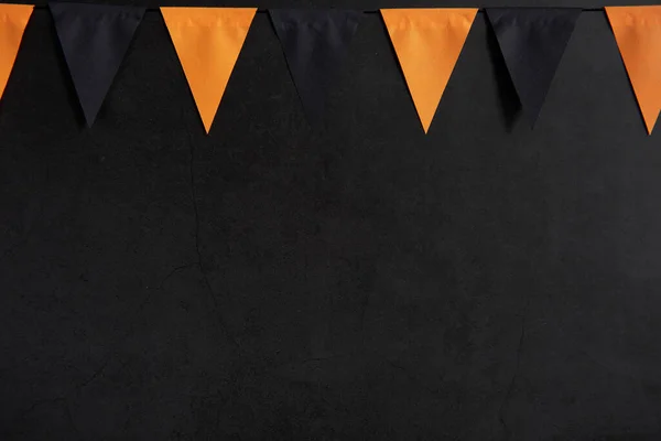 Halloween garland of black and orange flags on a dark background with space for text.
