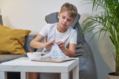 Elinde fırça olan bir çocuk kağıt hamuru için bir parça kağıt yapıştırıyor. Çocuk ev ödevi için dağ şeklinde yaratıcı bir proje yapıyor. Kağıtçı mache