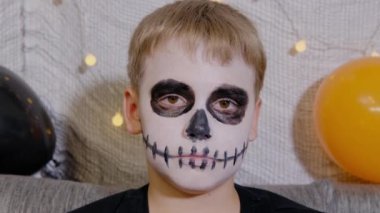 Cadılar Bayramı 'nda yüzünde iskelet şeklinde makyajı olan bir çocuğun yakın plan portresi. Çocuk şeker mi şaka mı tatiline hazır. Kameraya bakıyorum.