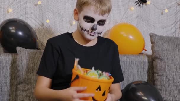 スケルトンメイクの男の子がハロウィンパーティーからキャンディーを取り出します 10月の祭りの季節 — ストック動画