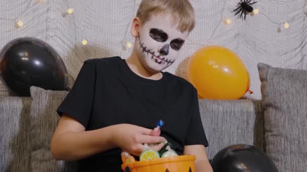 スケルトンメイクの男の子はキャンディーのバケツを持っています 子供はハロウィンを祝う — ストック動画