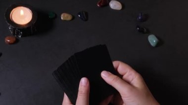 Bir kadının el ele tutuşup, bir deste kağıt karıştırdığı yakın plan. Tarot kartlarının yardımıyla ezoterikizm ve geleceği tahmin etmek