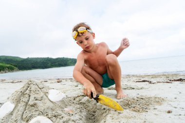 Deniz kabuklarıyla kumdan kule inşa eden sevimli çocuk yaz mevsiminde tropikal tatil köyünde kürek kemiği kullanıyor.