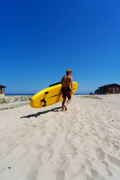 Активний чоловічий серфер, що працює з дошкою для серфінгу на піщаному пляжі, насолоджуючись здоровим способом життя екстремальний спорт — стокове фото
