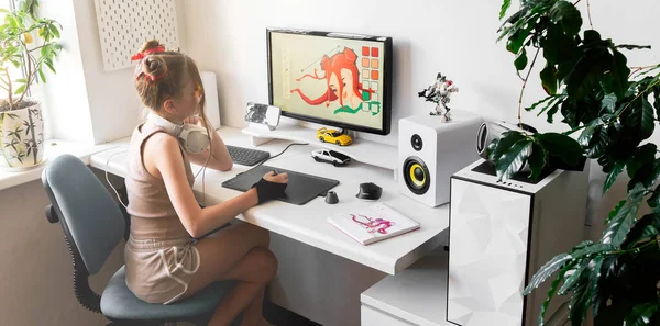 一个年轻的女孩在舒适的办公室里用图形片在电脑上画画. 图库图片