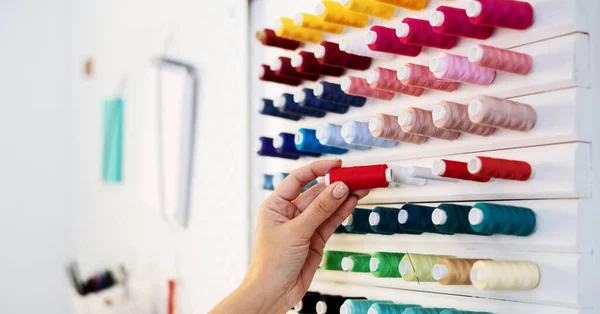 Una chica sastre selecciona hilos de colores para el trabajo de sastre. Primer plano de las manos — Foto de Stock