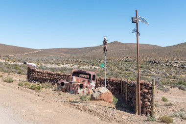 FRASERBURG, Güney Afrika - SEP 3, 2022: Karoo Burnu 'nun kuzeyinde Fraserburg ve Sutherland arasında tarihi Posta Yolu üzerinde Kruisrivier çiftliğinin girişindeki yol manzarası. Karikatürler ve eski bir araba enkazı görünür.