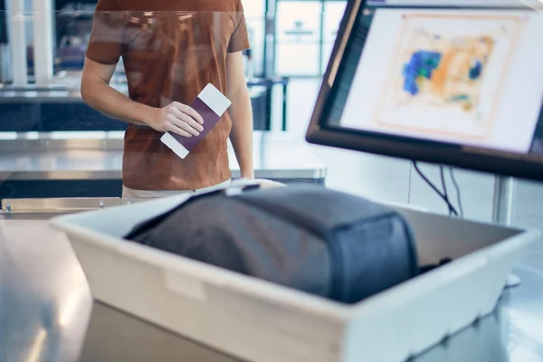 Airport security check. Young man waiting for x-ray control his bag