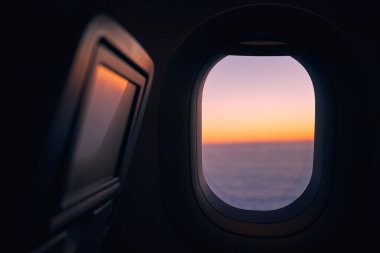 Güzel günbatımında bulutların üzerinde uçarken uçağın penceresi. 