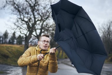 Kasvetli yağmurlu bir günde kırık şemsiyeyi kuvvetli rüzgarda tutan adam. Temalar hava ve meteoroloji. 