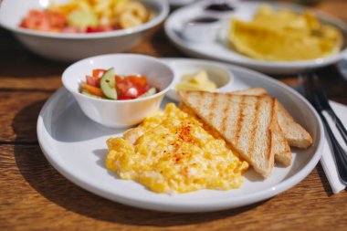 Tahta masada kahvaltı çeşitleri. Çırpılmış yumurta, kızarmış ekmek ve sebze salatasına yakından bak.