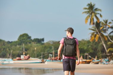 Kum kıyısında balıkçı tekneleriyle yürüyen bir adam. Sri Lanka 'da sırt çantalı turistin arka görüntüsü