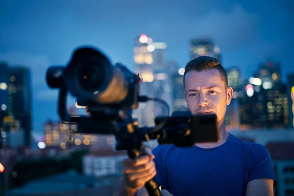 カメラとジンバルで撮影する男 夜のライトアップされた都市のスカイラインに対するビデオ作家の肖像 — ストック写真