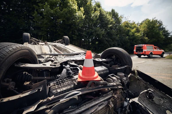 Damaged car on the roof after accident against fire rescue vehicle. Selective focus on traffic cone