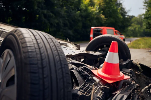 Damaged car on the roof after accident against fire rescue vehicle. Selective focus on traffic cone