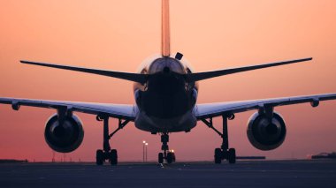 Rear view of airplane taxiing to runway for take off. Traffic at airport at dawn.