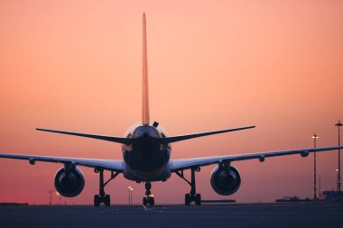Rear view of airplane taxiing to runway for take off. Traffic at airport at dawn.