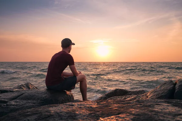 人们坐在岩石上观看大海上田园诗般的日落的后视镜 — 图库照片
