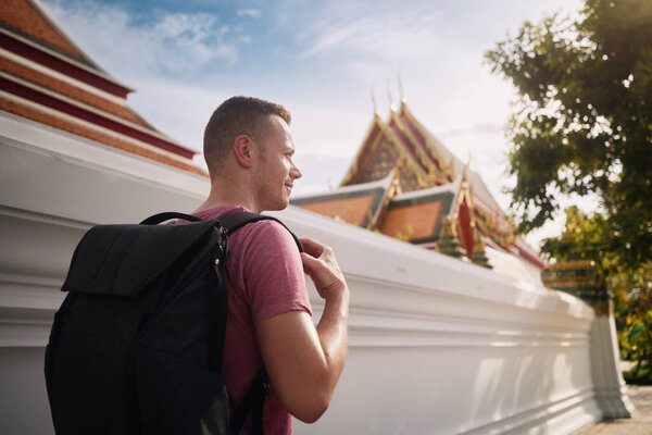 Tourist with backpack walking on street against Buddhist temple. Bangkok, Thailand