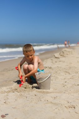 Boy playing with sand at the beach clipart