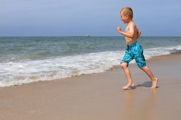 Poika juoksee kohti merta — kuvapankkivalokuva