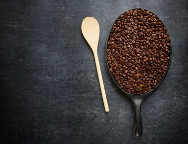 Kahve kızartma konsepti, ahşap karıştırma kaşığı ve kavrulmuş kahve çekirdekleriyle kızartma tavası, yakın çekim, üst manzara