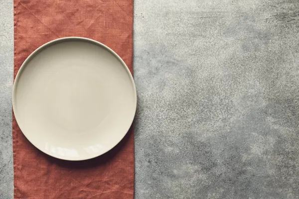 灰色纹理混凝土背景设计与米黄色空食物盘在梯形亚麻布餐巾纸上 复制空间 免版税图库图片