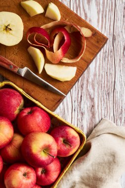 Sepetteki kırmızı elmalar ve kesme tahtasındaki elmalar turta yapmak için soyuluyor.