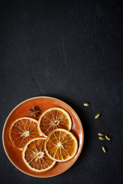 Plate with dried orange slices with badjan and cardamom on black slate background with copy space