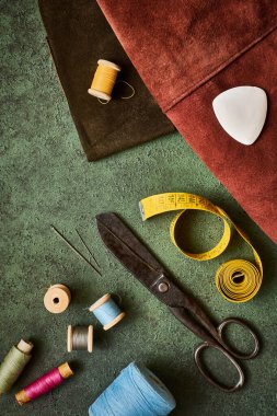 Dikiş malzemeleri, antika makas, iplik makaraları, ve yeşil desenli arka plan terzileri, düz yatıyordu