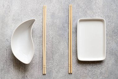 White empty plates and bamboo chopsticks on gray background with copy space