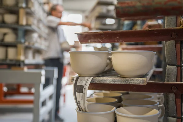 陶器工場の棚の上のカップと背景の労働者 — ストック写真