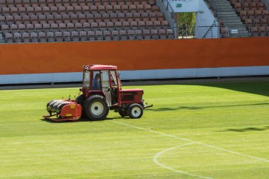 Traktörlü bir adam stadyumda futbol sahasını havalandırıyor..