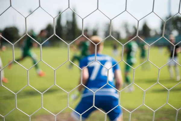 Detail of goal\'s post with net and football goalkeeper in the background.