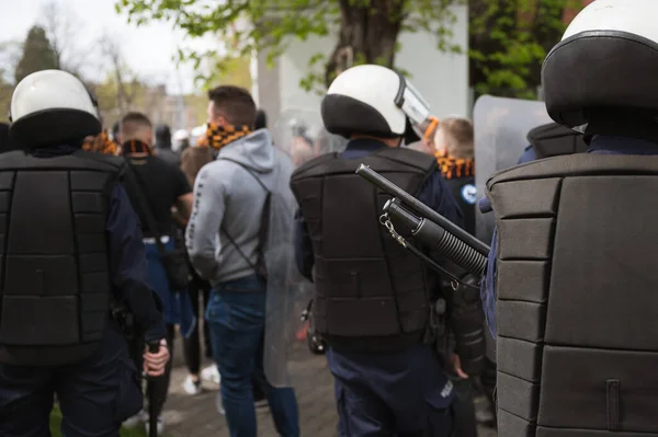 Police rifle barrel and masked people in the background.