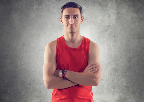 Портрет мускулистого молодого спортсмена, одетого в красную майку, руки скрещенные на серой текстурированной бетонной стене — стоковое фото