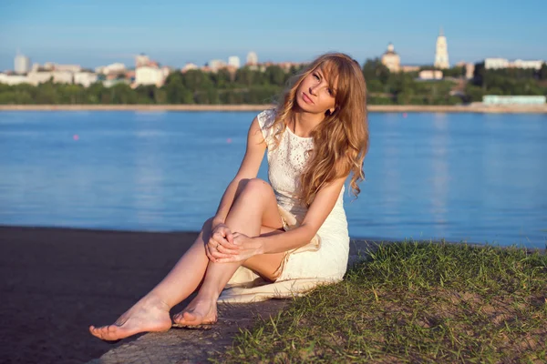 Soleado al aire libre retrato de encantadora chica romántica con el pelo largo bajo el atardecer. Tarde de verano Atractiva joven sentada en la playa cerca de un río. Foto estilo tonificado filtros de Instagram — Foto de Stock