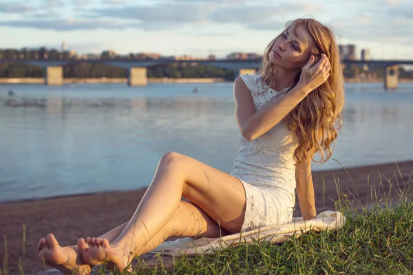 Soleado al aire libre retrato de encantadora chica romántica con el pelo largo bajo el atardecer. Tarde de verano Atractiva joven sentada en la playa cerca de un río. Foto estilo tonificado filtros de Instagram — Foto de Stock