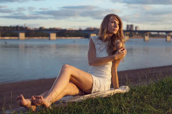 Soleado al aire libre retrato de encantadora chica romántica con el pelo largo bajo el atardecer. Tarde de verano Atractiva joven sentada en la playa cerca de un río. Foto estilo tonificado filtros de Instagram — Foto de Stock