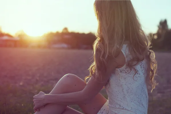 Sonniges Porträt einer schönen jungen romantischen Frau oder eines Mädchens in weißem Kleid am Strand, das den Sonnenuntergang beobachtet und den Sommerabend in der Natur genießt. Weiches Licht. Sonnenschein. getönte warme Farben. — Stockfoto